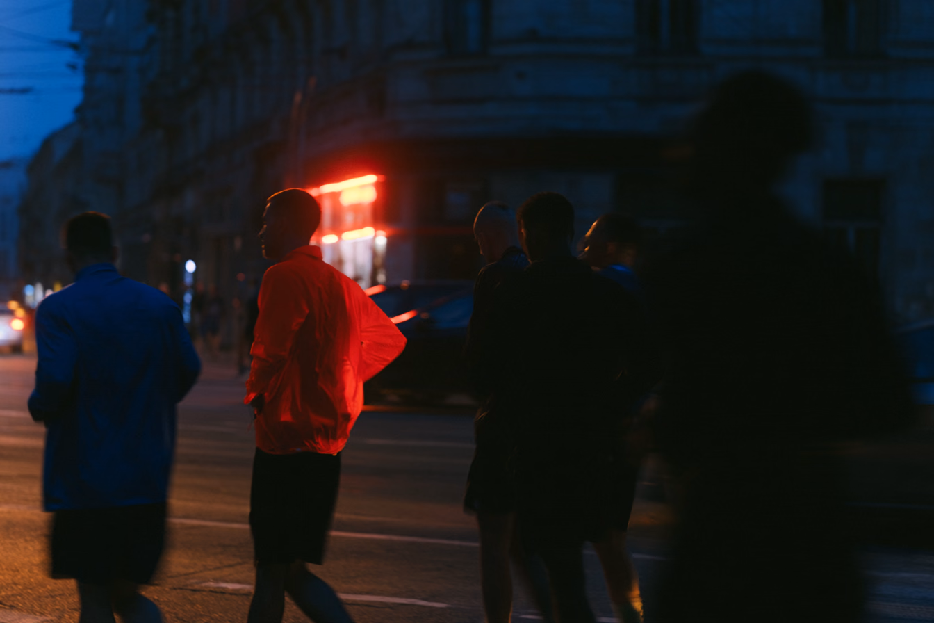 Members crossing a city street at night, one in a red jacket